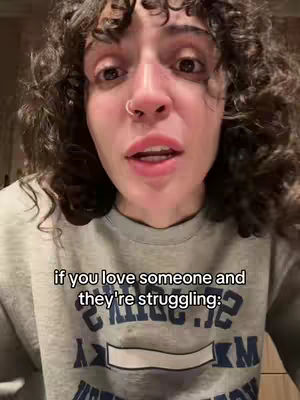 A close-up shot of a woman with curly brown hair and a nose ring. She is looking directly at the camera and speaking. The text overlay at the bottom says: "if you love someone and they're struggling:"