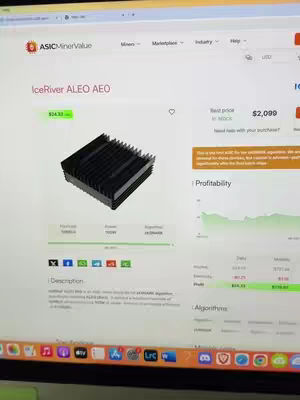 A computer screen displays a website focused on crypto mining hardware, showcasing a black, rectangular ASIC mining device, a graph of profitability, and other data related to the hardware in the background.