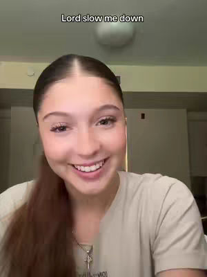 A smiling young woman with long brown hair poses in front of a plain background. The text 'Lord slow me down' is overlaid at the top.