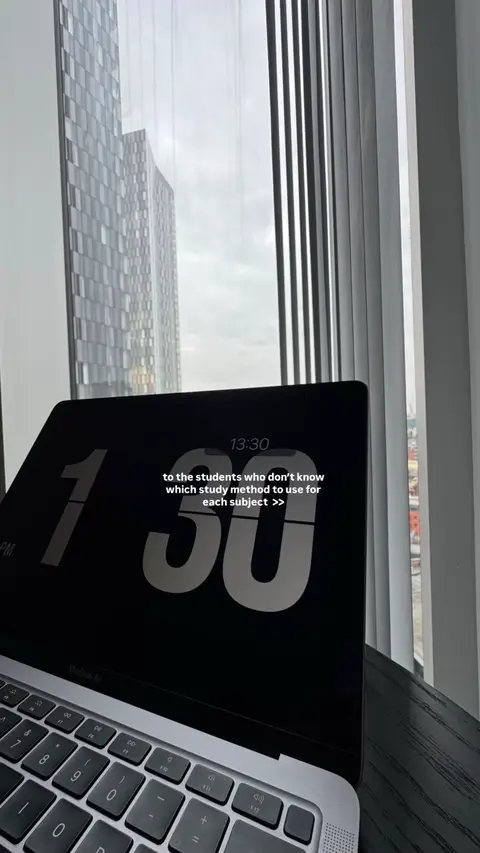A laptop with the time displayed on the screen sits on a dark wooden surface, beside a large window with a view of tall buildings outside. The laptop screen prominently displays the time as 1:30 above the text.