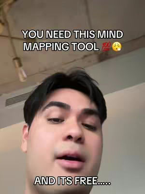 A selfie-style shot of a young man with dark hair against a neutral-colored backdrop. He is looking directly at the camera. Above him, text overlays in a black font state: "YOU NEED THIS MIND MAPPING TOOL 100 ". Below him, in the same font, it reads, "AND ITS FREE.....".