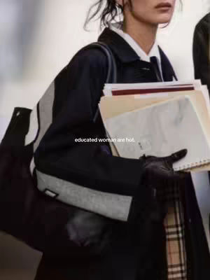 The image shows a woman from the shoulders up, carrying papers and a tote bag with a light background. She's dressed in a coat and a white shirt and tie. the hook "educated woman are hot" is added on the cover image.