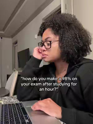 A woman with curly hair and glasses sits in front of a laptop, propping her head up with her hand. Text overlayed on the image asks how to get a 98% on exams after studying for only an hour.