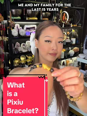 The cover image features a medium shot of a woman holding up two Pixiu bracelets towards the camera. She's positioned slightly off-center, with the bracelets prominently displayed in the foreground. The background adds depth, revealing shelves lined with various objects, suggesting a store or a personal collection. A red rectangular graphic with white text stands out on the lower left corner of the image.