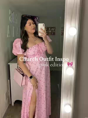 A woman self-records in a well-lit room with a large mirror. She wears a light pink dress with a floral pattern and holds a smartphone in front of her face. Text is overlaid on the image reading 'Church Outfit Inspo (pink edition)' with a pink bow graphic, suggesting fashion or outfit ideas.