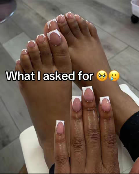 The image displays a close-up view of hands and feet with freshly manicured nails. The nails have a square shape with a pale pink color and a white tip. The image is well-lit, showing details of the skin and nails. In the foreground are hands, and in the background are feet with similar nail art. Text overlayed states 'What I asked for' with two emojis: a distressed face and a crying face.