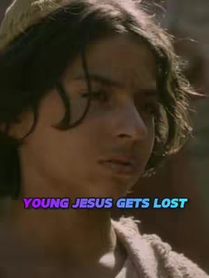 A close-up shot featuring the face of a young boy, presumably playing the role of Jesus, with dark curly hair and a serious expression. The background is blurred, suggesting a scene from a historical drama or film.