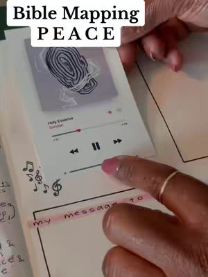 A person's hands holding an open journal or notebook, with a transparent cover over a page displaying a digital music player interface. The cover also features superimposed text. A finger with pink nail polish points to an element on the music player interface. Additional elements include handwritten notes and musical notes.