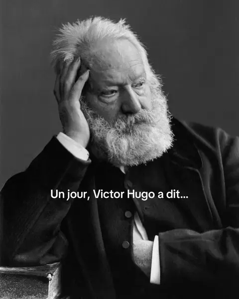 A black and white, medium shot of Victor Hugo, an older man with a large, white beard and tousled hair, in deep thought. The background is a muted gray. Text overlayed on the image reads, "Un jour, Victor Hugo a dit..."