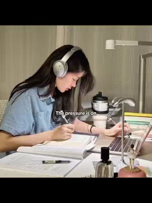 The cover image shows a woman with long dark hair wearing headphones and a light blue shirt, focused on studying at a desk. She is writing in a notebook with a pen in her right hand, while a laptop and other study materials are spread out on the desk. The background includes a simple wall and a bright lamp.