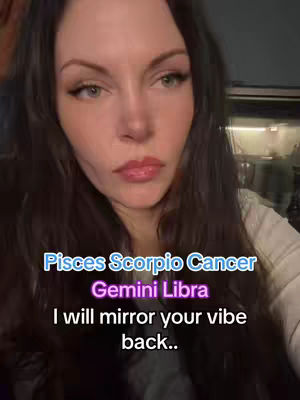 A frontal shot of a woman with long brown hair and fair skin, looking directly at the camera. The background is a blurred interior, and overlaid text identifies zodiac signs and the phrase 'I will mirror your vibe back..'.
