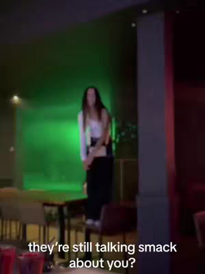 The cover photo shows a dimly lit interior with a woman standing on a chair in front of a green-lit background. She is wearing a white top and dark pants. Text overlays are added at the bottom.