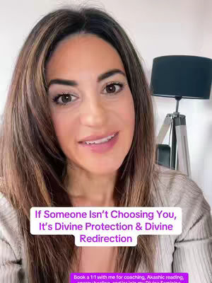 A woman with brown hair and a light-colored top smiles directly at the camera. A text overlay reads, "If Someone Isn't Choosing You, It's Divine Protection & Divine Redirection." A lamp is visible in the background.