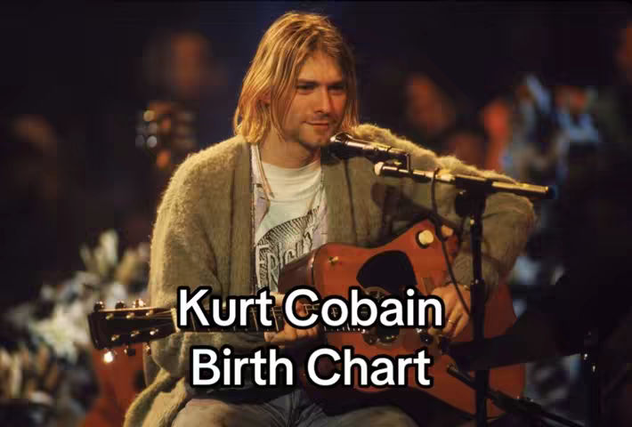 The cover image features a medium shot of Kurt Cobain playing an acoustic guitar and singing into a microphone. The text overlay is white and says 'Kurt Cobain Birth Chart' in a bold, sans-serif font against the bottom center of the image. Behind Cobain is a dark background, with muted colors.