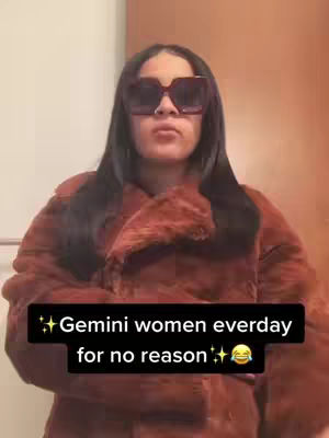 The image shows a woman with long, black hair and large sunglasses, wearing a fur-looking brown coat. The image is framed from the chest up, standing in front of what appears to be a bathroom door. A text overlay in a black box reads "Gemini women everyday for no reason" with sparkly emojis.