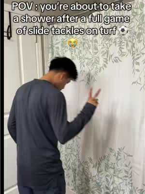 A young man, viewed from the back and side, stands in a bathroom. He's wearing a dark long-sleeved shirt. The shower curtain behind him has a pattern of leaves. He has his right hand held up in a peace sign. Text is overlaid at the top.