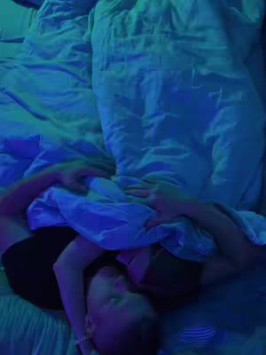 The cover image shows two figures in bed, illuminated by a blue light. The figures are embracing, their faces close together, with the angle looking down on them.