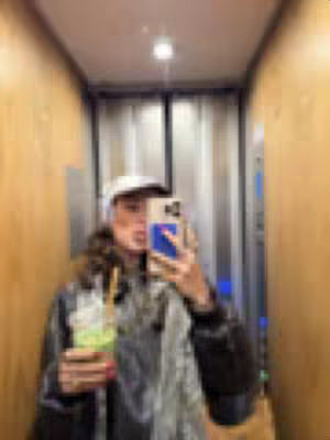 A person is taking a selfie in an elevator. The person is holding a phone up showcasing a reflection of their face and surroundings including a drink. The elevator has wooden paneling.