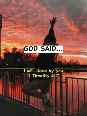 The image captures a person from the back with their arm raised towards a colorful sunset. The person is standing on a bridge-like structure with a metal railing, and there's text overlayed that reads "GOD SAID..." and a scripture. The background features a vibrant sky with hues of orange and red.