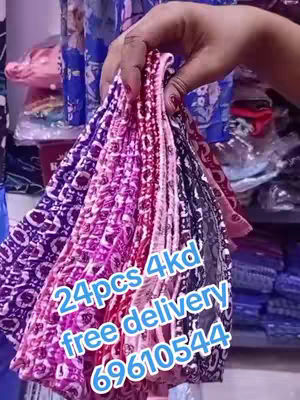 A hand holds a large collection of colorful headbands or scrunchies. The items are primarily shades of pink, purple, and black, arranged in a layered, fan-like display. The background is somewhat blurred, showing shelves of other items. Text overlaid on the image advertises a sale with a phone number.