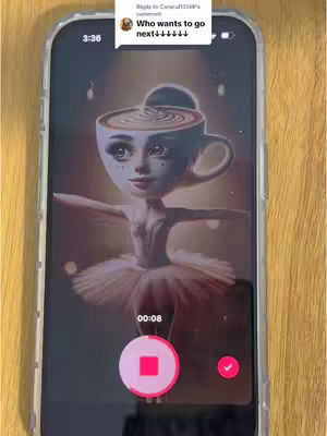 The image shows a smartphone displaying a digital art piece. The art depicts a ballerina whose head is replaced by a coffee cup with a latte art design. The ballerina is wearing a tutu. On the phone's screen, there's also an interface with a red record button and a checkmark, indicating a video recording or editing interface. The upper portion has a speech bubble saying, 'Who wants to go next?' Text elements over the phone screen inform the time.