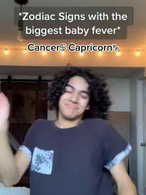 The cover image shows a young man with dark curly hair, making a slight smirk. Above him is text that states, "Zodiac Signs with the biggest baby fever", and below is the Cancer and Capricorn zodiac signs. Behind the man, the background shows a bedroom setting lit up with string lights.