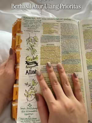 The cover image showcases open pages of a Bible, with a person's hands holding and interacting with the pages. The upper text overlay says "Berhasil Atur Ulang Prioritas". The left page has handwritten notes and drawings, one of the drawings depicts a vine and leaves, and the text below is written in a stylized font. The right page contains highlighted text. The setting appears to be a bed based on the background.