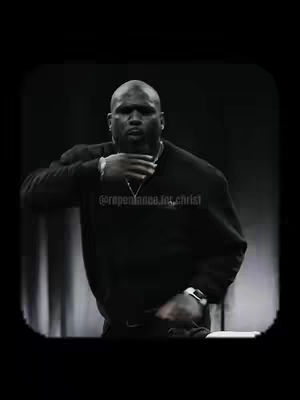 A grayscale medium shot features a bald Black man, dressed in a black sweater, with his right hand touching his neck. He is the focal point, positioned centrally against a blurred background, with a subtle watermark indicating the video's theme. The lighting is soft, and the composition emphasizes seriousness.