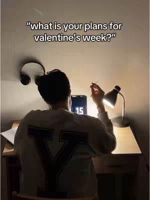 The image shows a person sitting at a desk, viewed from behind. The person is wearing a sweatshirt with a large letter 'Y' on the back. A lamp is lit on the desk, and a tablet displaying the number '15' is also present. Headphones hang on the wall above, and text overlays the image.