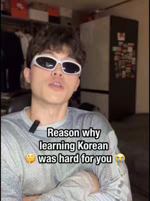 A young man wearing white sunglasses is in the center of a video cover image. The man is looking up slightly, and a text overlay stating the reason why learning Korean was hard is placed on his chest.