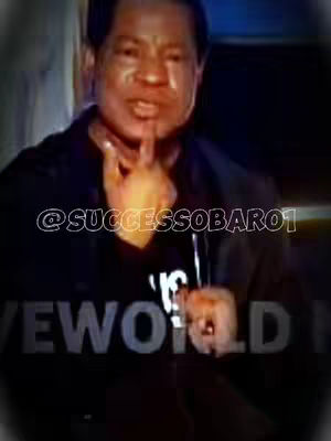 A medium shot shows a man with short hair, wearing a black jacket over a white t-shirt with text, holding up his hand, and touching his chin with one finger. Overlay text indicates the content's author and branding.