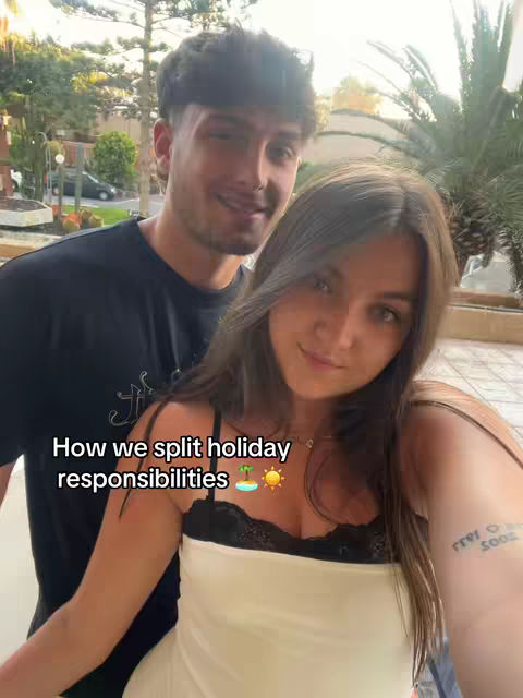 A selfie-style shot featuring a couple posing closely together, likely outdoors, given the background of greenery and a building. The woman is in the foreground, wearing a white top, her arm with a tattoo is visible. The man is positioned slightly behind her, casually dressed and smiling at the camera. Text overlay at the bottom conveys the video's theme.