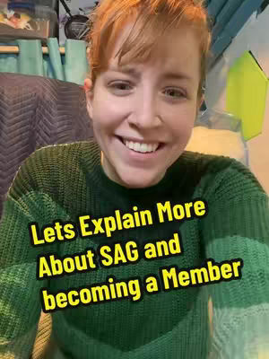 A smiling woman with fair skin and red hair is the central focus. She wears a dark green sweater. Overlayed text in a yellow outlined box reads, "Lets Explain More About SAG and becoming a Member". The background is slightly blurred, suggesting the image was taken indoors..