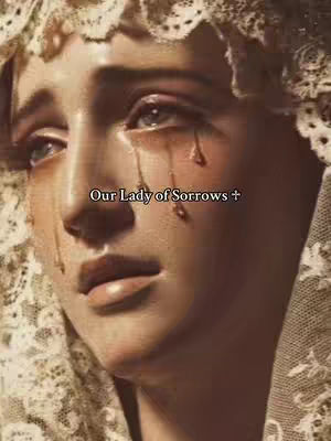 A close-up portrait of a statue of Mary, featuring a sorrowful expression, with tears streaming down her face. She wears a white veil adorned with lace. Overlay text 'Our Lady of Sorrows +' is visible. The image is in warm tones, with a shallow depth of field.
