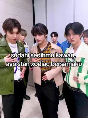 A group of young men are posing indoors. The central figure is wearing a beige jacket over a patterned sweater. Text has been added to the image.