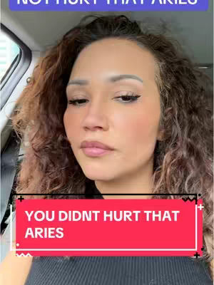 A woman with curly brown hair is seated inside a vehicle, likely a car, and is the primary focus. She's looking towards the camera with a neutral expression. The woman's complexion is fair, and she wears makeup, including eyeliner and blush. A red rectangle is overlaid at the bottom covering part of the woman. The background is blurred, with hints of what appears to be a car interior and a window.