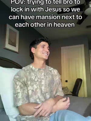 A young man is seated indoors, smiling slightly, with text overlaid. The background suggests a bedroom setting with a bed, a framed picture, and a door. He is wearing a patterned shirt and light-colored pants. The overall composition is well-lit, with a casual and friendly vibe.