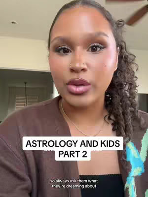 A woman with curly hair and makeup is centered in the frame, looking forward. A white text box at the bottom reads, 'ASTROLOGY AND KIDS PART 2'. Below, smaller text states 'so always ask them what they're dreaming about'. The overall composition is well-lit and focuses on the speaker's face.