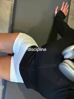 The cover image features a person lying on a textured surface, wearing white athletic shorts and black leggings. The word “discipline” is superimposed on the image in the lower center. The person’s arm is extended with the hand resting on a surface. Gray exercise equipment of unknown use can be seen on the right. The image is shot at a slight angle, providing a view of the person's torso and legs. The colors are muted, with a focus on black and white.
