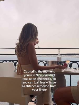 A woman sits at a table with a glass of rosé, enjoying a scenic view of the ocean from a balcony. Text overlay provides context for the scene.