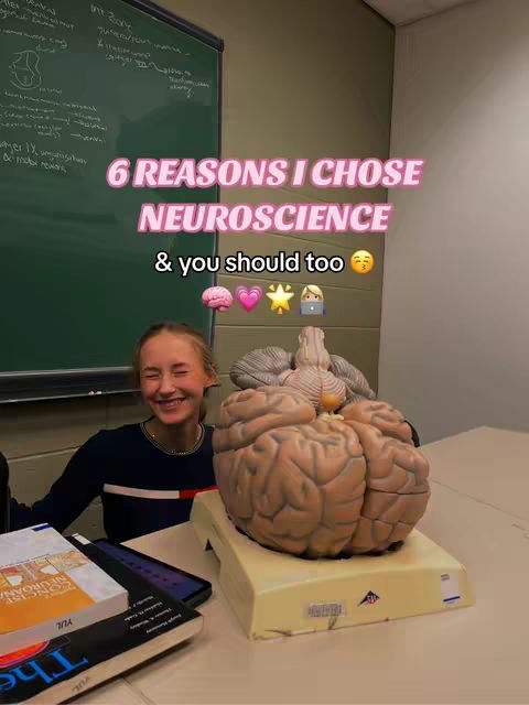 A smiling young woman is positioned in front of a table with a large brain model. In the background is a whiteboard with handwritten notes and a section of wall. The foreground features books and a tablet on the table, suggesting a study or educational environment. The image has a warm, inviting tone.