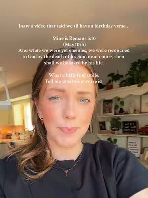 A woman with long brown hair and blue eyes, wearing a black shirt and a necklace with a cross pendant, is the central focus of a selfie-style video. The background suggests a residential setting, with a shelf filled with various items including what seem to be framed pictures. The lighting is soft, and the overall composition is simple, highlighting the woman's face and the overlaid text.
