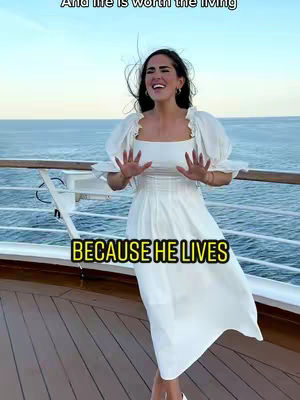 A woman in a white dress is standing on a ship deck with the ocean behind her; text overlay says "BECAUSE HE LIVES".