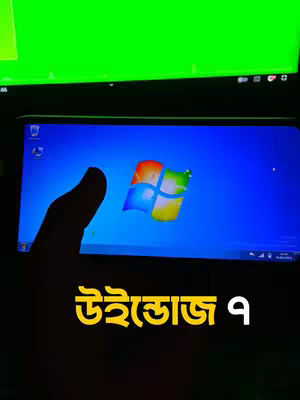 A hand holding a mobile phone displaying a Windows OS interface. Over the image is Bangla text in a bold, yellow font. The background is largely dark but displays a green monitor and a secondary phone, possibly a device used to record the screen display.
