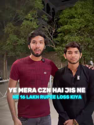 Two men stand side-by-side in front of a blurred background of trees and a building. The man on the left wears a maroon t-shirt and the man on the right wears a black shirt. Text with a white background is overlaid on the lower portion of the video.