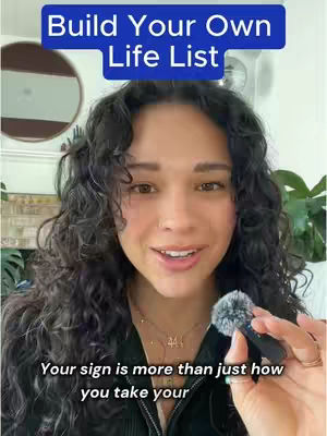 A woman with long, dark, wavy hair is centered in the frame, smiling slightly while holding a microphone. A blue banner that reads 'Build Your Own Life List' is at the top. Text overlays the bottom, and in the background, objects are slightly visible, set against a soft focus.