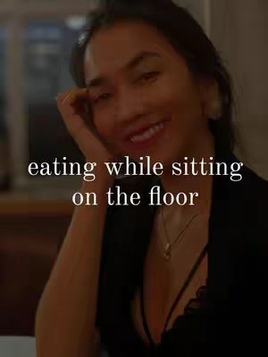 The cover image features a woman with dark hair smiling at the camera while resting her chin on her hand. Text overlayed in the image reads, 'eating while sitting on the floor'. The background is blurred, suggesting an indoor setting.