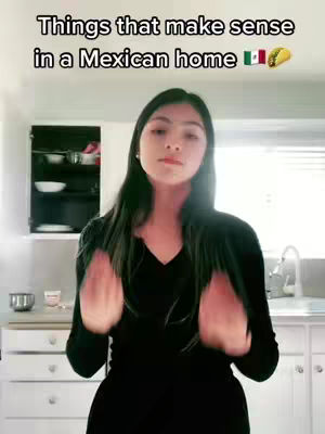 A woman stands facing the camera in a kitchen setting. Above her head is text. She's wearing black, and her arms are up doing hand gestures in the foreground. The image has a bright, neutral color palette.
