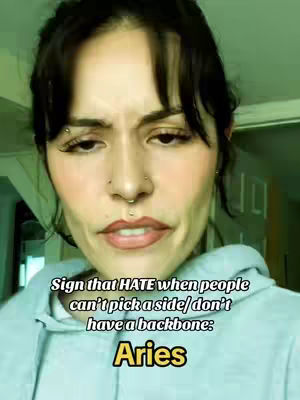 A close-up shot of a woman with dark hair and multiple facial piercings. Text overlays with a black background and a golden Aries zodiac are in the bottom.