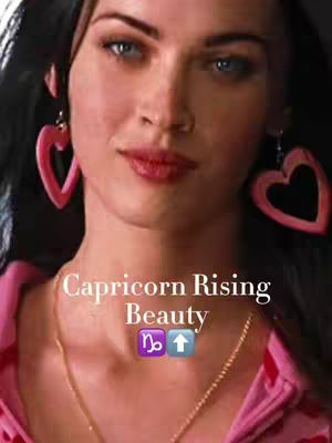 The cover image features a close-up of a woman's face. She has dark hair and is wearing large, pink heart-shaped earrings. Her lips are glossed, and she has a golden necklace. The text overlay reads 'Capricorn Rising Beauty' with symbols below. The overall composition is vibrant and focuses on beauty and astrological themes.